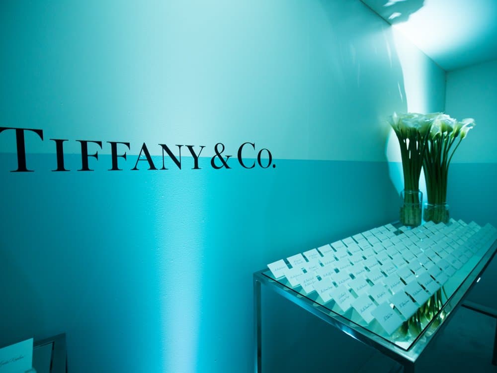 Escort cards laid out on a mirrored table beneath calla lilies and the Tiffany & Co. wordmark