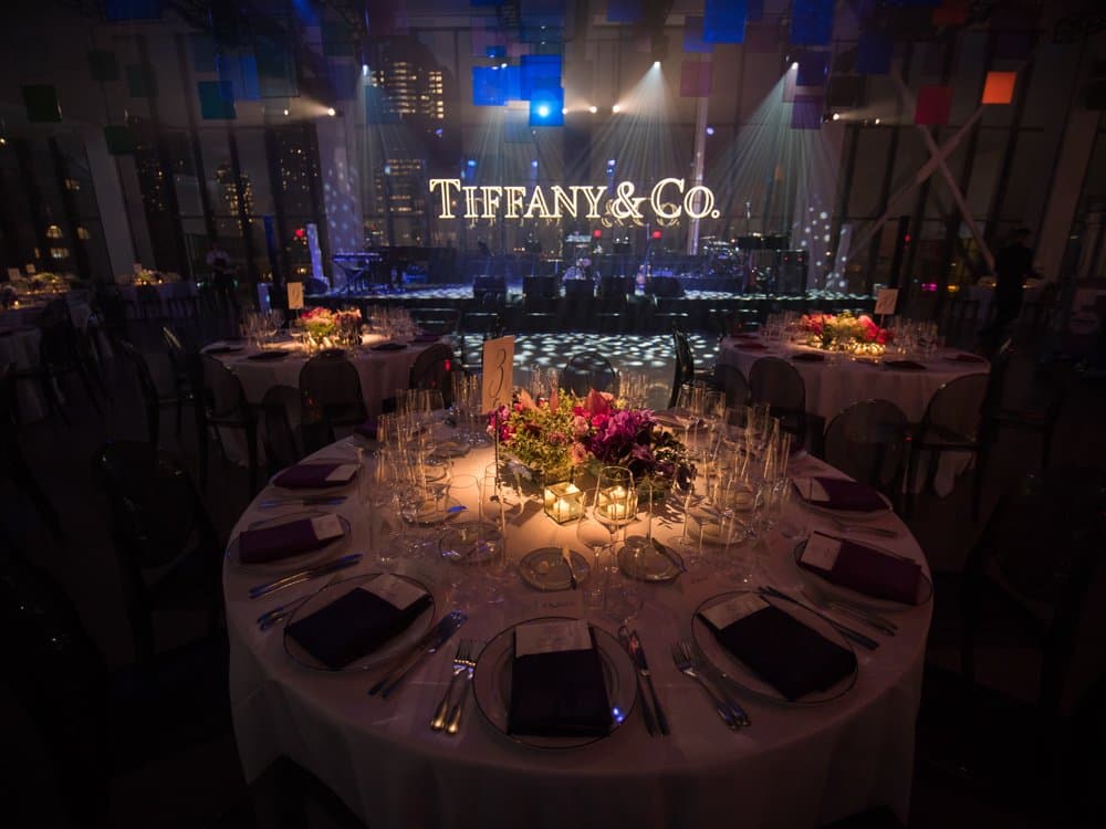 Set dinner tables and a lit stage at a Tiffany & Co. gala, with the New York skyline behind