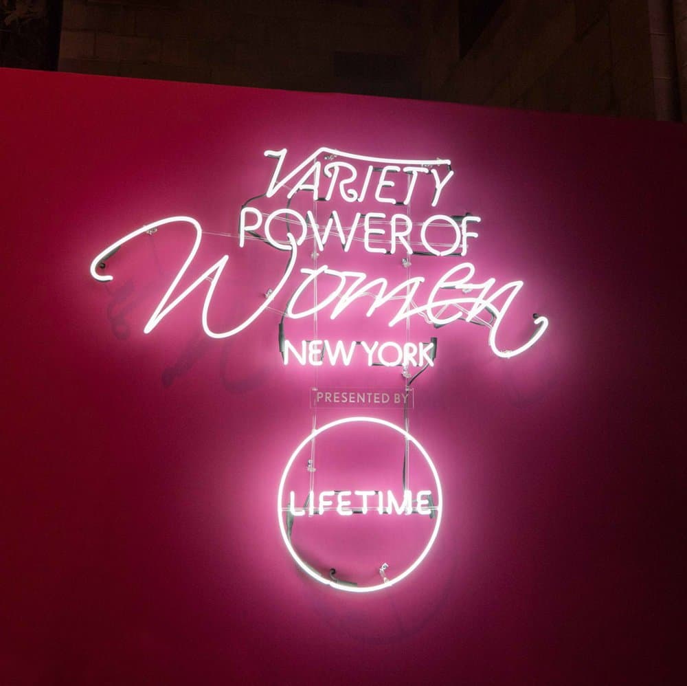 A neon Variety Power of Women New York sign, presented by Lifetime, on a magenta wall
