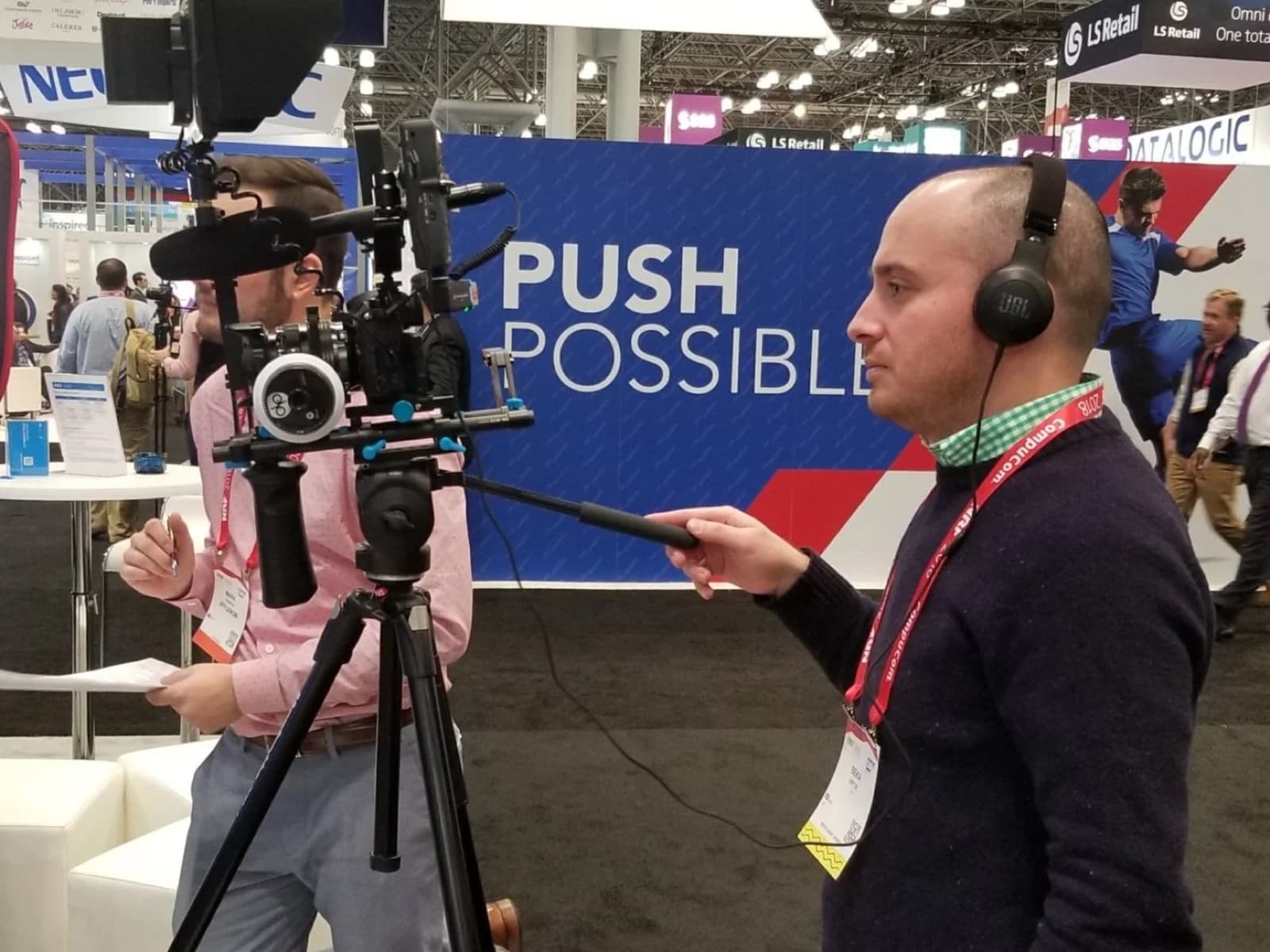 Operator monitoring audio on headphones beside a rigged camera on the show floor