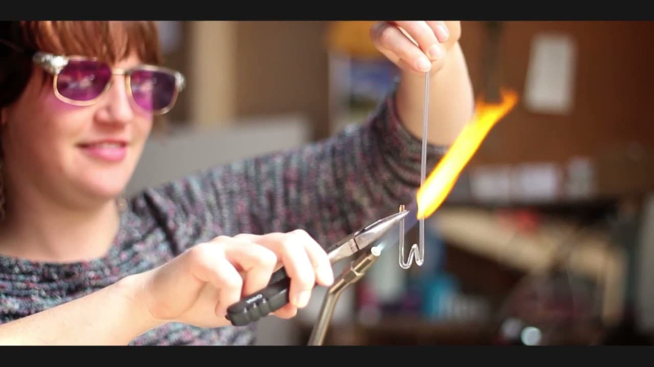 A torch flame shaping a small glass link held in pliers, from Glass Chains